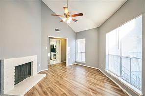 3724 Woodchase Dr, Houston, TX 77042 - unfurnished living room with a ceiling fan, wood finished floors, a fireplace with raised hearth, and high vaulted ceiling
