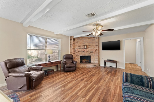 9602 Philmont Dr, Houston, TX 77080 - living area with beamed ceiling, a textured ceiling, light wood-style flooring, ceiling fan, and a brick fireplace