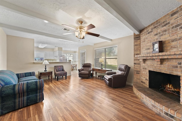9602 Philmont Dr, Houston, TX 77080 - living room with a textured ceiling, wood finished floors, a brick fireplace, a ceiling fan, and beamed ceiling