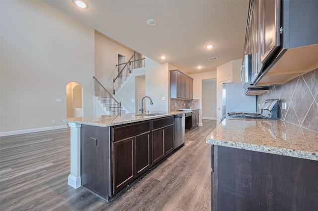 14538 Bending Maple Dr, Houston, TX 77069 - kitchen with stainless steel appliances, wood finished floors, arched walkways, dark brown cabinets, and tasteful backsplash