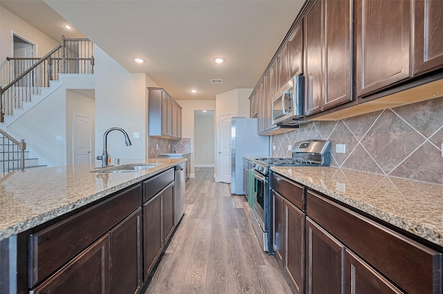 14538 Bending Maple Dr, Houston, TX 77069 - kitchen featuring stainless steel appliances, light wood finished floors, light stone counters, dark brown cabinets, and decorative backsplash