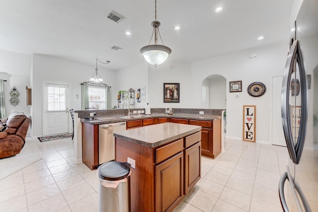 17906 Keenan Cv, Houston, TX 77084 - kitchen with appliances with stainless steel finishes, a kitchen island, brown cabinetry, arched walkways, and light tile patterned floors