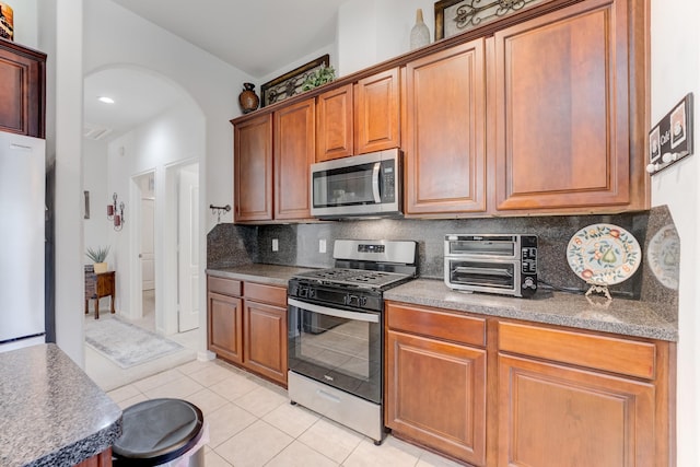 17906 Keenan Cv, Houston, TX 77084 - kitchen with appliances with stainless steel finishes, light tile patterned flooring, arched walkways, tasteful backsplash, and brown cabinets