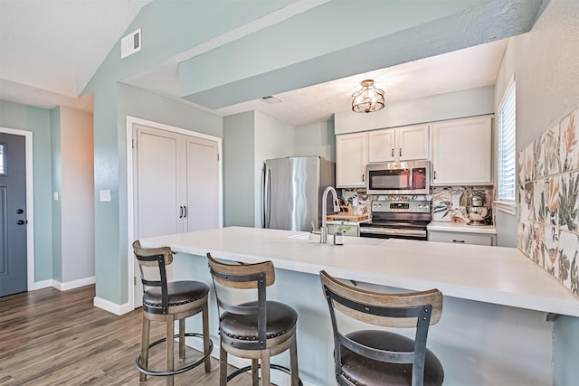 4023 Spanish Main Blvd, Galveston, TX 77554 - kitchen featuring appliances with stainless steel finishes, a breakfast bar area, wood finished floors, decorative backsplash, and light countertops