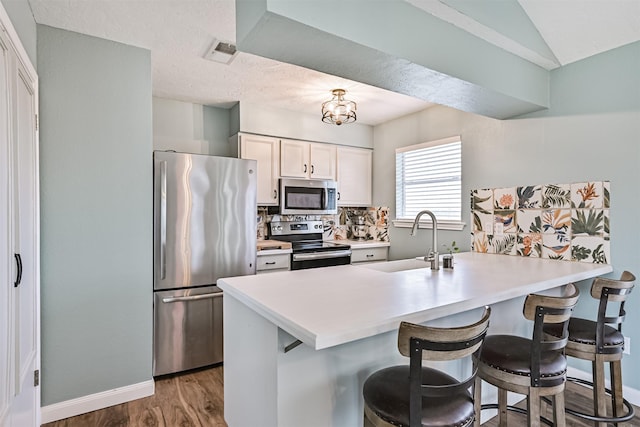 4023 Spanish Main Blvd, Galveston, TX 77554 - kitchen with appliances with stainless steel finishes, a breakfast bar area, white cabinets, wood finished floors, and a peninsula