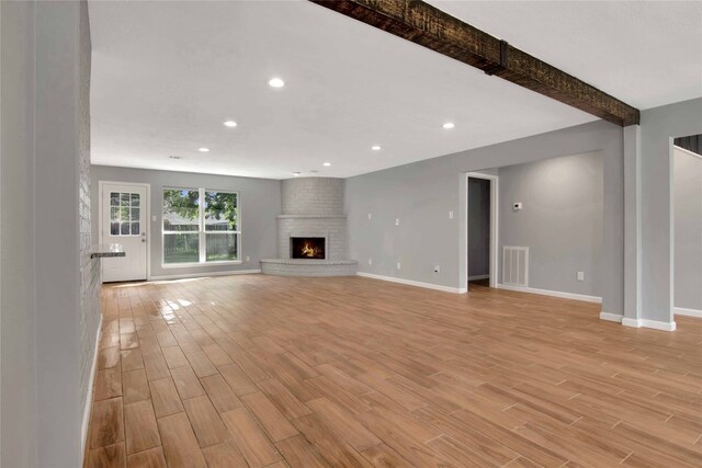 12811 Golden Tee Ln, Houston, TX 77099 - unfurnished living room with light wood-type flooring, recessed lighting, beamed ceiling, and a brick fireplace