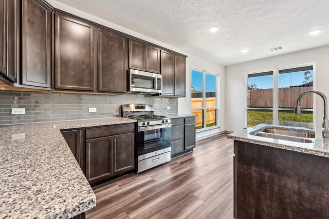 1418 Lake Ridge Dr, Brenham, TX 77833 - kitchen with stainless steel appliances, dark brown cabinetry, wood finished floors, light stone counters, and backsplash