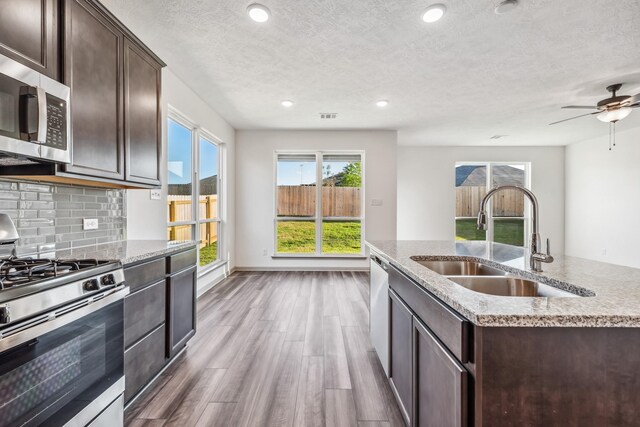 1418 Lake Ridge Dr, Brenham, TX 77833 - kitchen featuring appliances with stainless steel finishes, dark brown cabinetry, wood finished floors, a textured ceiling, and backsplash