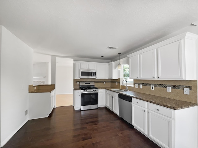 7007 Madison Trl, Houston, TX 77084 - kitchen featuring stainless steel appliances, dark wood-style floors, white cabinets, decorative backsplash, and pendant lighting