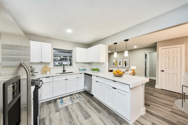 5817 Beechnut St, Houston, TX 77074 - kitchen with stainless steel appliances, a peninsula, light countertops, light wood-style floors, and white cabinetry