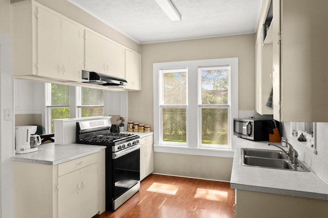 213 E Feagin St, Livingston, TX 77351 - kitchen featuring appliances with stainless steel finishes, under cabinet range hood, light wood-style floors, light countertops, and white cabinetry