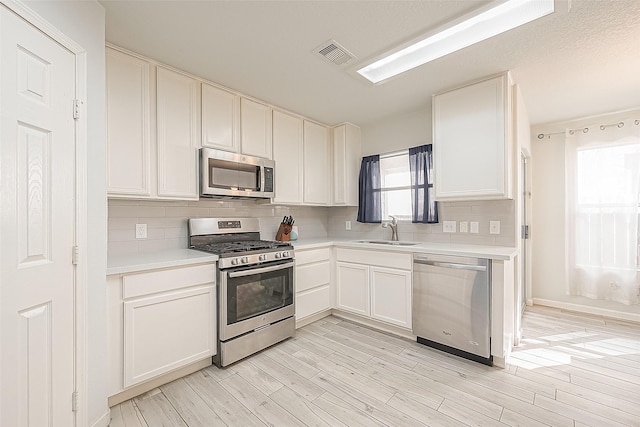 2335 Village Leaf Dr, Spring, TX 77386 - kitchen with appliances with stainless steel finishes, light countertops, decorative backsplash, light wood finished floors, and white cabinetry
