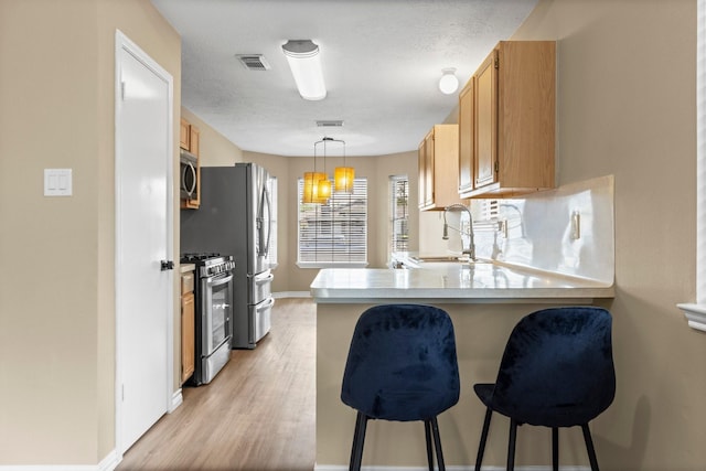 29222 Waltham St, Spring, TX 77386 - kitchen with appliances with stainless steel finishes, a peninsula, light countertops, a kitchen bar, and light wood-style flooring