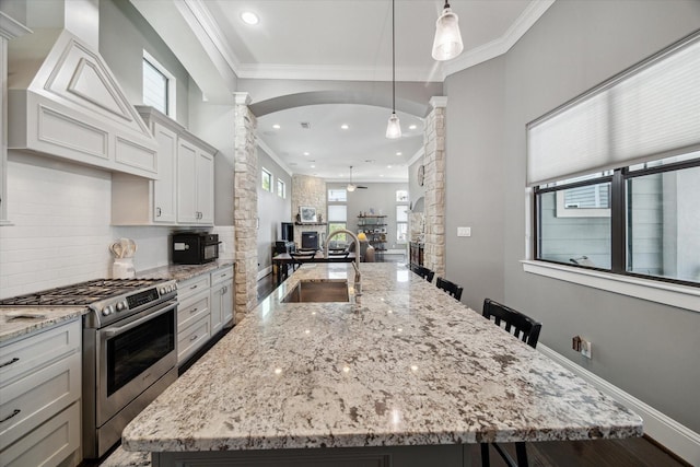 1219 W 25th St Unit A, Houston, TX 77008 - kitchen featuring stainless steel range with gas cooktop, decorative columns, a kitchen island with sink, crown molding, and arched walkways