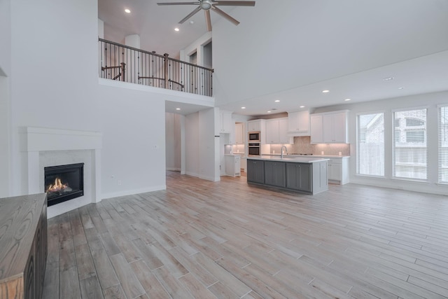 17010 Harpers Way, Conroe, TX 77385 - unfurnished living room featuring ceiling fan, light wood-style floors, a glass covered fireplace, recessed lighting, and a high ceiling
