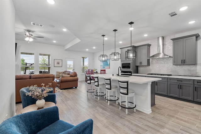 1224 Garden Jade Dr, Katy, TX 77493 - kitchen featuring wall chimney range hood, open floor plan, gray cabinets, built in microwave, and a breakfast bar