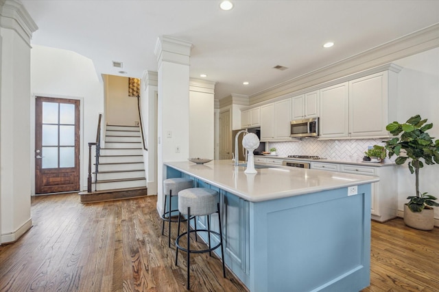 1518 Dunlavy St, Houston, TX 77006 - kitchen featuring stainless steel microwave, a breakfast bar area, backsplash, wood finished floors, and light countertops