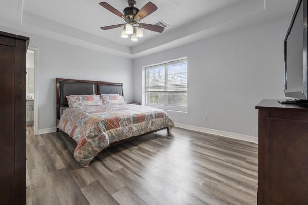 19602 Hardwood Ridge Trl, Cypress, TX 77429 - bedroom with a tray ceiling, wood finished floors, a ceiling fan, and a barn door