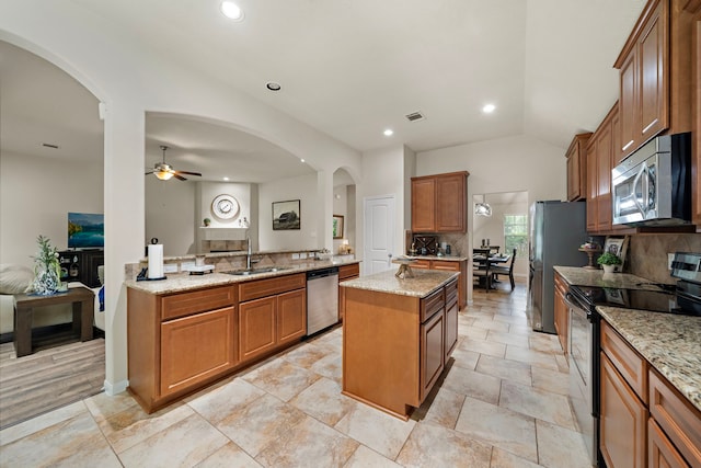 12311 Hawthorne Dr, Montgomery, TX 77356 - kitchen with appliances with stainless steel finishes, arched walkways, a kitchen island, brown cabinetry, and ceiling fan