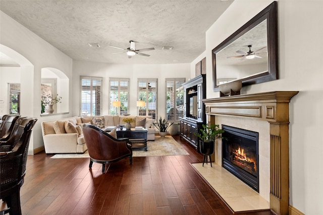 12902 Tamarack Bend Ln, Humble, TX 77346 - living area with ceiling fan, a fireplace, dark wood-style floors, arched walkways, and a textured ceiling