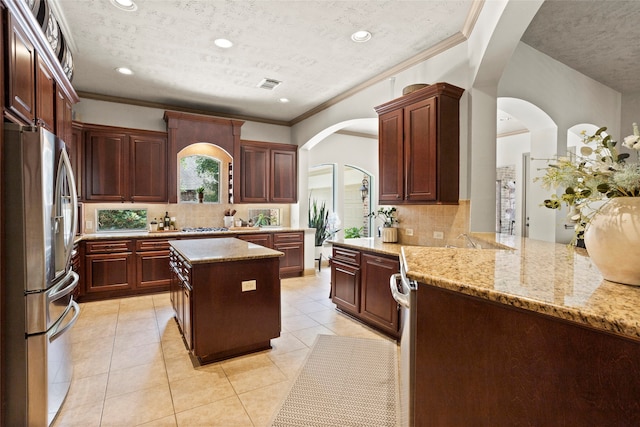 12902 Tamarack Bend Ln, Humble, TX 77346 - kitchen featuring freestanding refrigerator, arched walkways, tasteful backsplash, a textured ceiling, and light stone counters