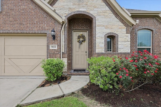 9111 Regan Way, Mont Belvieu, TX 77523 - view of exterior entry with brick siding, a garage, concrete driveway, and stone siding