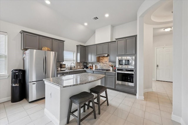 9111 Regan Way, Mont Belvieu, TX 77523 - kitchen featuring appliances with stainless steel finishes, under cabinet range hood, a center island, tasteful backsplash, and vaulted ceiling