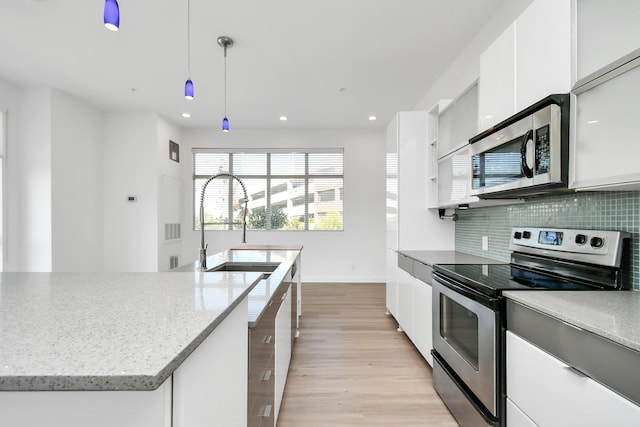 207 Pierce St Unit 301, Houston, TX 77002 - kitchen featuring stainless steel appliances, light wood-style flooring, white cabinetry, backsplash, and light stone countertops