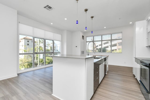 207 Pierce St Unit 301, Houston, TX 77002 - kitchen with appliances with stainless steel finishes, an island with sink, light wood-type flooring, recessed lighting, and white cabinets