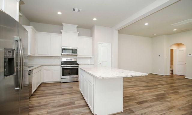 239 Biltmore Loop, Montgomery, TX 77316 - kitchen with appliances with stainless steel finishes, a center island, tasteful backsplash, arched walkways, and light wood-style flooring