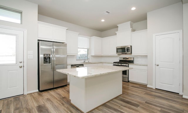 239 Biltmore Loop, Montgomery, TX 77316 - kitchen with appliances with stainless steel finishes, a kitchen island, decorative backsplash, white cabinetry, and wood finished floors