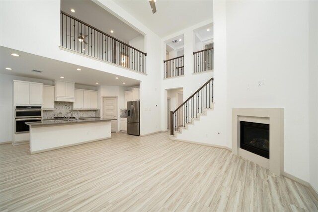 29423 Red Rocks Park Dr, Katy, TX 77494 - unfurnished living room with a fireplace, a high ceiling, light wood-type flooring, recessed lighting, and stairs