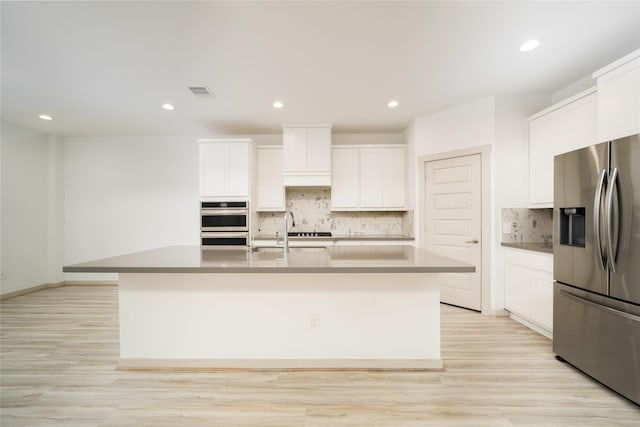 29423 Red Rocks Park Dr, Katy, TX 77494 - kitchen featuring appliances with stainless steel finishes, a kitchen island with sink, white cabinetry, decorative backsplash, and light wood finished floors