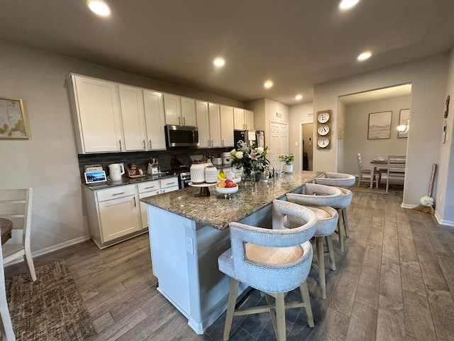 11711 Colossal Oak Dr, Houston, TX 77066 - kitchen with stainless steel microwave, dark wood finished floors, white cabinets, recessed lighting, and a kitchen breakfast bar