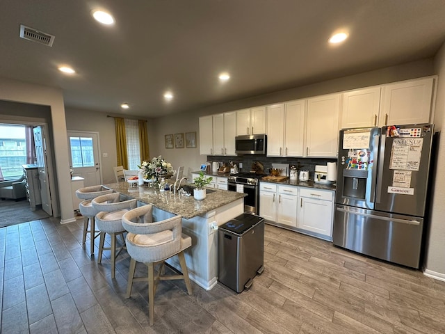 11711 Colossal Oak Dr, Houston, TX 77066 - kitchen with stainless steel appliances, wood finished floors, white cabinetry, a kitchen bar, and decorative backsplash