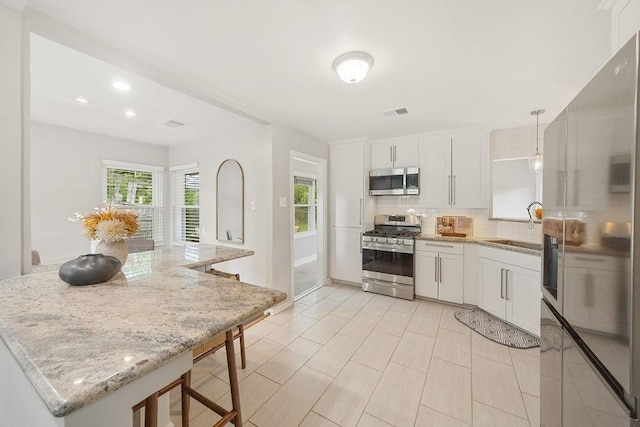 4502 Lido Ln, Houston, TX 77092 - kitchen featuring appliances with stainless steel finishes, backsplash, white cabinetry, light stone counters, and a breakfast bar area