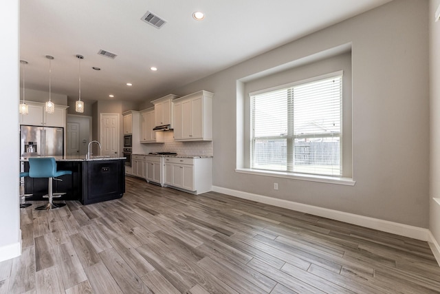 10318 Easterly Ln, Cypress, TX 77433 - kitchen with appliances with stainless steel finishes, a kitchen bar, white cabinets, light wood-type flooring, and tasteful backsplash
