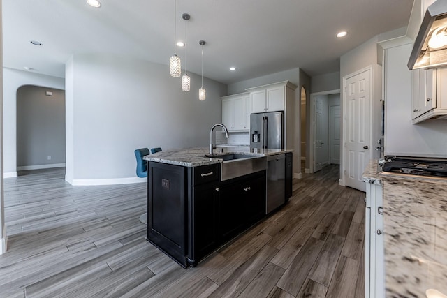 10318 Easterly Ln, Cypress, TX 77433 - kitchen featuring stainless steel appliances, a kitchen island with sink, wood finished floors, wall chimney exhaust hood, and dark cabinets