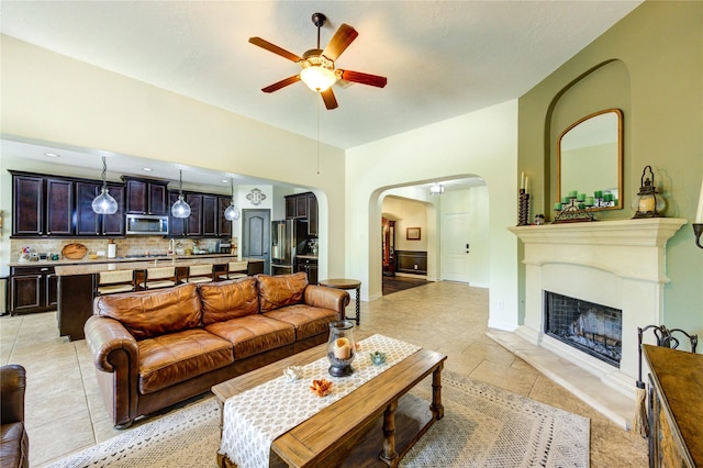 7003 Fall Creek Ln, Missouri City, TX 77459 - living room featuring arched walkways, a ceiling fan, light tile patterned floors, and a fireplace with raised hearth