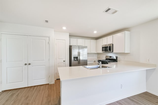 17427 Cyprian Cedar Ln, New Caney, TX 77357 - kitchen with stainless steel appliances, light wood-style flooring, light countertops, a peninsula, and white cabinets