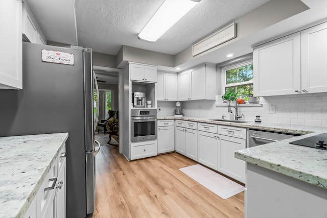 24111 Norchester Way, Spring, TX 77389 - kitchen with stainless steel appliances, light wood-type flooring, decorative backsplash, white cabinetry, and light stone countertops