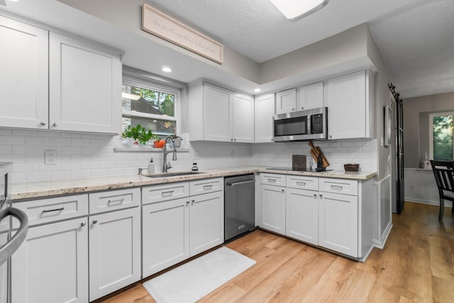 24111 Norchester Way, Spring, TX 77389 - kitchen featuring stainless steel appliances, white cabinets, decorative backsplash, light wood-style floors, and light stone counters