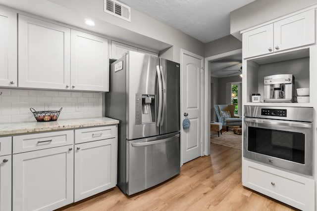 24111 Norchester Way, Spring, TX 77389 - kitchen with stainless steel appliances, light wood-type flooring, white cabinetry, decorative backsplash, and light stone counters