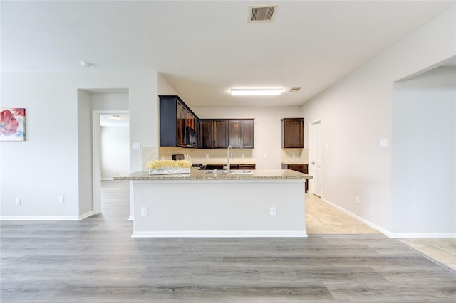 9207 Ranch Ridge Ln, Richmond, TX 77407 - kitchen with dark brown cabinetry, light wood-type flooring, light stone countertops, and backsplash
