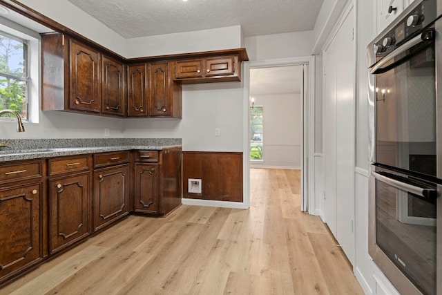6515 Pebble Beach Dr, Houston, TX 77069 - kitchen featuring double oven, light wood-style floors, plenty of natural light, a wainscoted wall, and dark brown cabinets