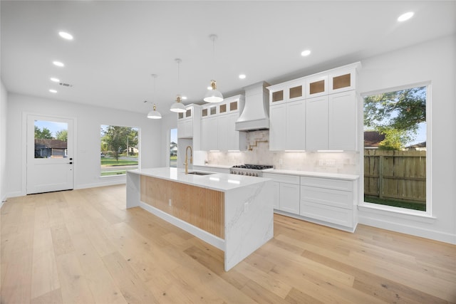 8646 Alcott Dr, Houston, TX 77080 - kitchen with premium range hood, decorative backsplash, a center island with sink, light wood-style floors, and white cabinetry