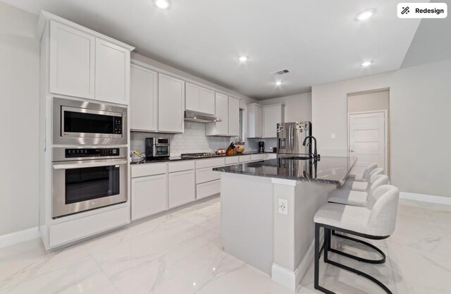8922 Granary Gate Ln, Richmond, TX 77407 - kitchen featuring stainless steel appliances, light marble finish floors, recessed lighting, a center island with sink, and backsplash