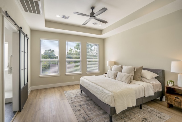 4101 E Rogers St, Houston, TX 77022 - bedroom with a barn door, a raised ceiling, light wood finished floors, ceiling fan, and recessed lighting