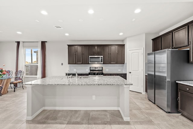 3506 Lake Bella Megan Dr, Katy, TX 77493 - kitchen featuring stainless steel appliances, a center island with sink, dark brown cabinets, light stone countertops, and recessed lighting