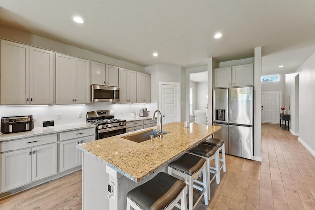 2231 Bright Sunrise Trl, Fresno, TX 77545 - kitchen with stainless steel appliances, light wood finished floors, a breakfast bar area, light stone counters, and an island with sink